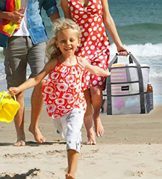 Woman on the beach with her family, holding loaded beach tote.